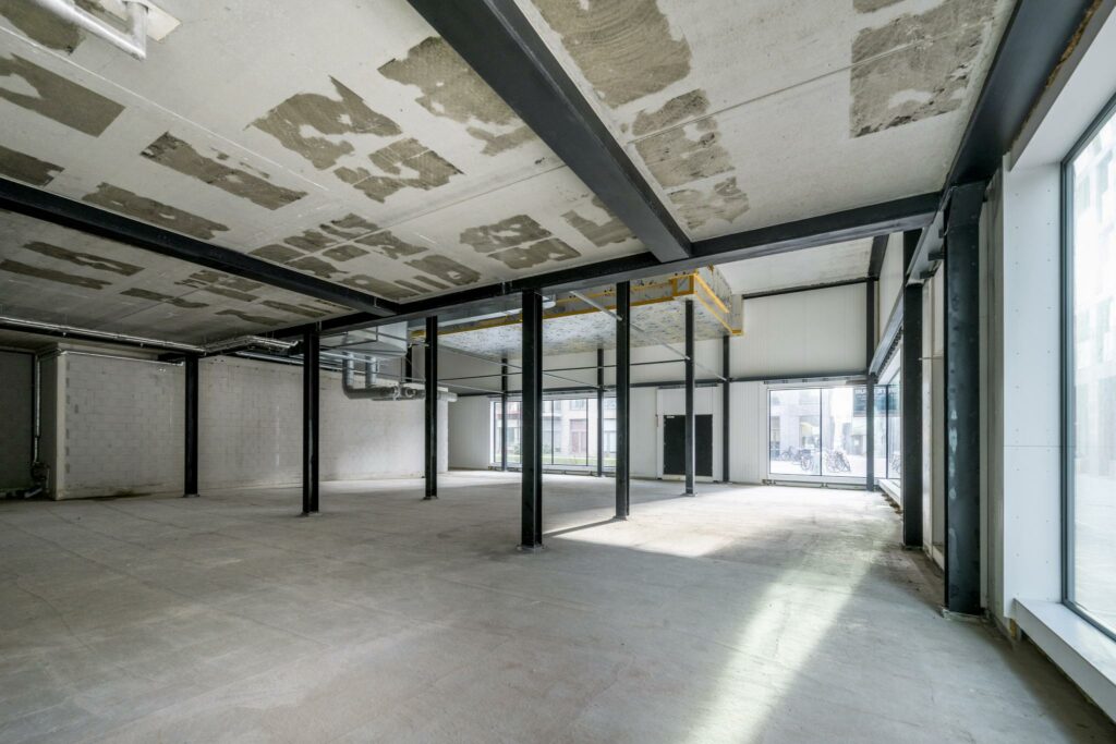 Leegstaand bedrijfs- of winkelpand aan de Pieter Goosstraat met betonnen vloer, plafond met staalconstructie en grote raampartijen.